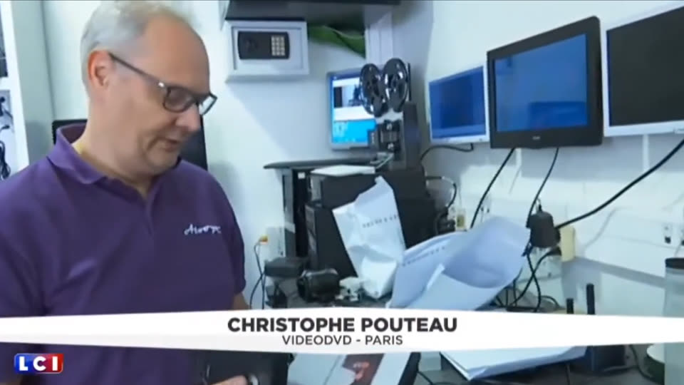 Christophe Pouteau, de VideoDVD, dans l'atelier parisien, devant un projecteur de bobines et des écrans de contrôle, pendant le reportage de LCI.